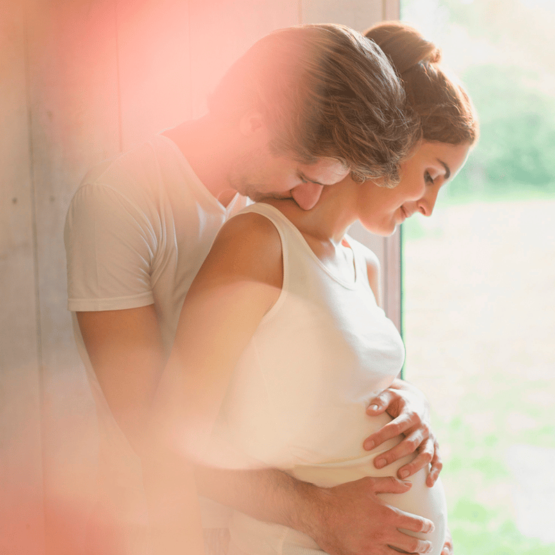 Fertilização in vitro e psicologia: Casal abraçado. Homem abraçando barriga da mulher, que está grávida.
